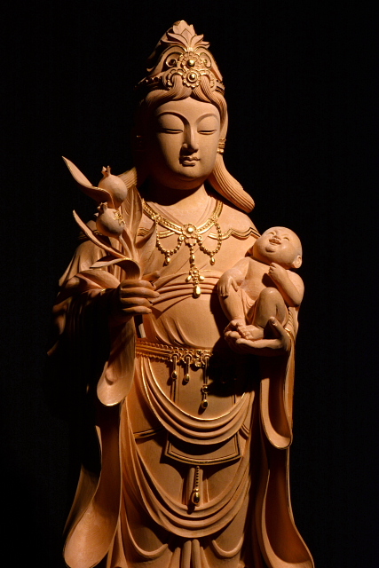 仏像彫刻原田謹刻 鬼子母神像(きしもじんぞう) 【鬼子母神】 仏法を守護する善女神。安産や育児の神。法華経護持の神ともされる。天女の姿をとり、左手に一子を抱き、右手には吉祥果を捧げる。ときには鬼神形のものもある。千人の子があったが、他人の子を取って食い殺したため、釈尊はその最愛の一児を隠してこれを教化し、のち仏に帰依して出産・育児の神となった。きしぼじん。訶梨帝母(かりていも)。ハーリティー。 【吉祥果】 鬼子母神が手に持つ魔除けの果実。なお吉祥果をザクロで表現するのは中国文化での影響であり、これは仏典が漢訳されたときに吉祥果の正体が分からなかったため、ザクロで代用表現したものである。